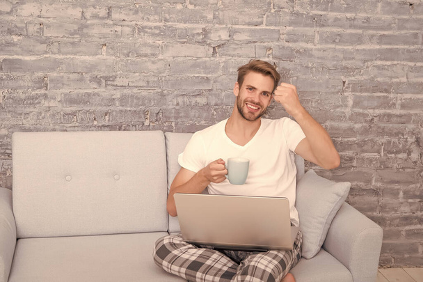 Distant Education. happy male on sofa. guy enjoying internet. social media addiction. computer addict. flirt and send text message. domestic lifestyle with mobile abuse. handsome man online dating - Фото, изображение