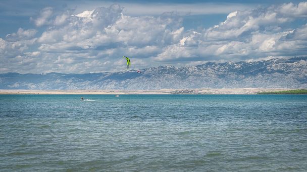 Вид с пляжа Здрияц между заливом Нин и Адриатическим морем на кайт-серфинг или кайтсерфинг с горным хребтом Динарических Альп на заднем плане, Хорватия - Фото, изображение