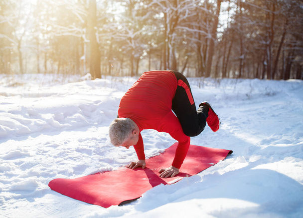 Fit senior man having outdoor yoga practice in winter at snowy forest - Photo, Image