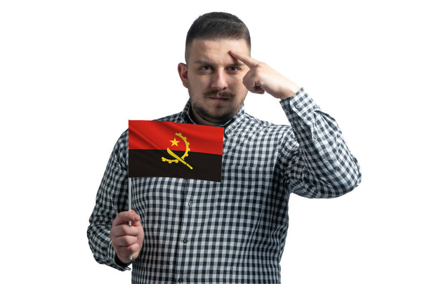 White guy holding a flag of Angola and a finger touches the temple on the head isolated on a white background. - Foto, imagen