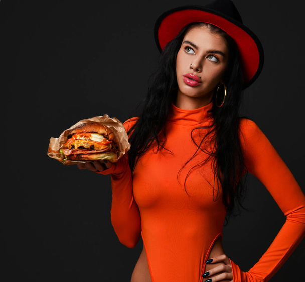 Sexy curvy woman with pouty lips in red body and hat holds on hand carries delivers served us big burger cheeseburger - Foto, afbeelding