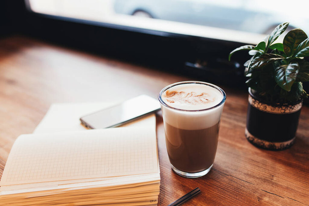 Чашка кофе, блокнот, телефон за столом в кафе. Размытый фон - Фото, изображение