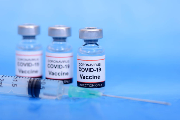 Aşı ve Sağlık Hizmetleri Tıbbi Konsepti. Korona virüsü enfeksiyonundan korunma, aşılama ve tedavi için mavi zemin üzerinde aşı ve şırınga - Fotoğraf, Görsel