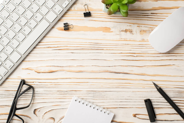 Acima da vista aérea foto de grampos de aglutinante suculento mouse caneta espiral teclado notebook na mesa de madeira branca com espaço em branco vazio no centro - Foto, Imagem