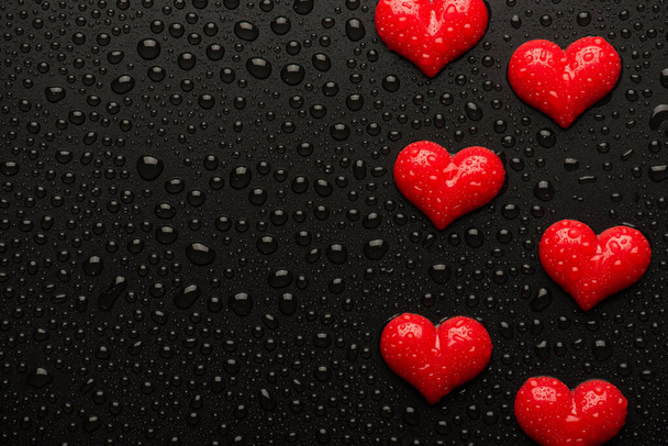 Top above overhead close up view photo image of red hearts on black backdrop with drops - Foto, imagen