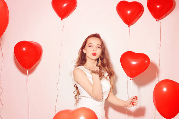 Valentine Beauty κορίτσι με μπαλόνια κόκκινο αέρα γέλιο, σε λευκό φόντο. Όμορφη Χαρούμενη Νεαρή γυναίκα. Ημέρα των γυναικών. Πάρτι διακοπών. Χαρούμενο μοντέλο ποζάρει, διασκεδάζει, χαμογελάει, γιορτάζει του Αγίου Βαλεντίνου. - Φωτογραφία, εικόνα