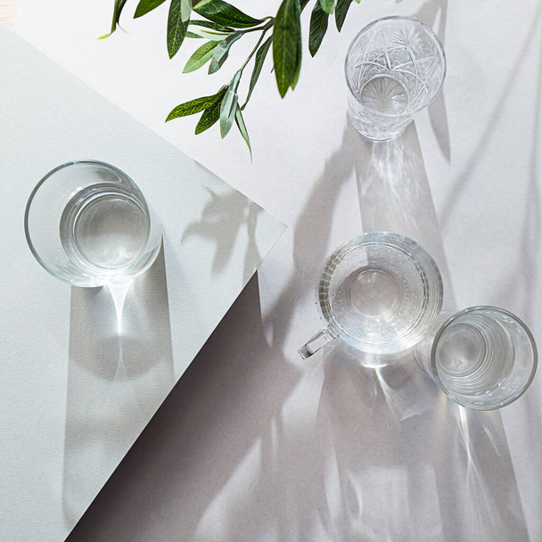 Склянки з водою зверху літня композиція на світлому фоні. Натюрморт з оливковою гілкою і довгими тінями, з копіювальним простором
 - Фото, зображення