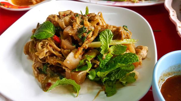 Spicy stir fried pickled bamboo shoots and belly pork with green mint leaves on top on white dish or plate at Thai local street food. Healthy diet and delicious food in Thailand and Asian meal - Photo, Image