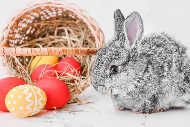 Cute rabbit and basket with Easter eggs on light background - Foto, afbeelding