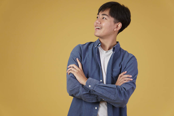 ritratto di felice bello giovane asiatico vestito casualmente con piegato incrociato braccia gesto isolato su studio giallo sfondo - Foto, immagini
