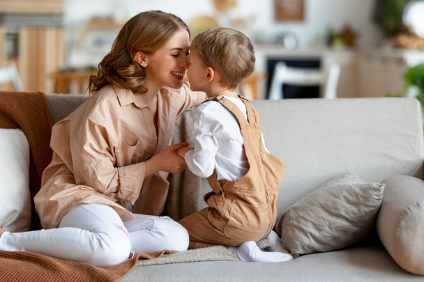 Mujer adulta encantada sonriendo y abrazando al niño mientras descansan en el sofá en casa juntos - Foto, imagen