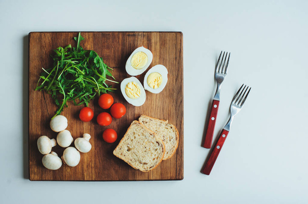 Ingredients for cooking vegetarian bruschetta with cherry tomatoes, ruccola, mushrooms and boiled eggs. Healthy diet breakfast - 写真・画像