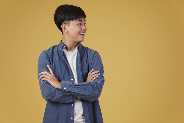 retrato de feliz guapo joven asiático hombre vestido casualmente con los brazos cruzados cruzados gesto aislado en amarillo estudio fondo - Foto, Imagen