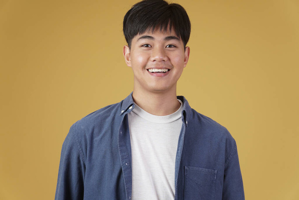 ritratto di sorridente felice allegro giovane uomo asiatico vestito casualmente isolato su sfondo studio giallo - Foto, immagini