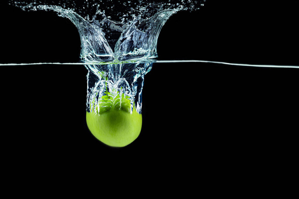Green apple falling in water with a splash against dark background - Fotó, kép