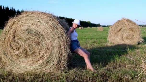 beautiful young girl in a hat pushes a haystack. Rural area. Feminist strong woman concept - Footage, Video