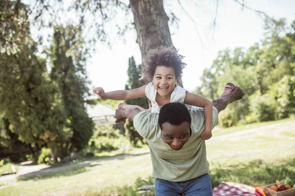 African american dad and his daughter having good time together in the park and feeling cheerful - Foto, afbeelding