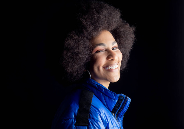 ziemlich gemischte Afro-Frau, lächelnd, in urbaner Kleidung glücklich lächelnd auf dunklem Hintergrund - Foto, Bild