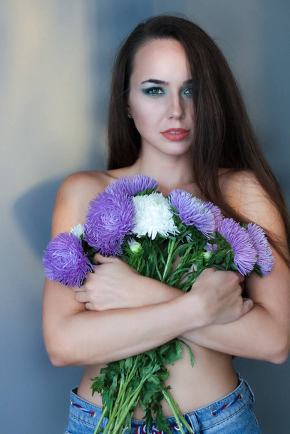 Beautiful young model, longhair girl with bright make-up, smoky eyes. Holding flowers - Photo, Image