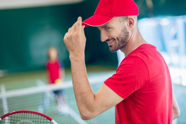 Waist up picture of a man in red cap playing tennis with a boy - Photo, Image