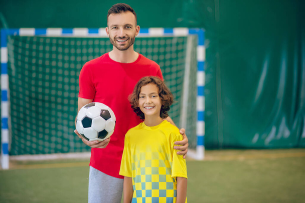PE teacher in red tshirt standing near his pupil and holding a ball - Photo, Image