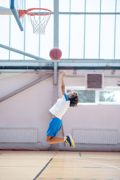 Dunkelhaariger Junge in Sportbekleidung bereit, den Ball in den Basketballring zu werfen - Foto, Bild