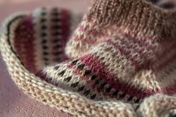 fragment van warm gestreepte raglan trui op roze betonnen ondergrond. Proces van het breien van merino wol, alpaca, doorweven draden van verschillende kleuren. Hygge gezellige sfeer van ambacht. Zachte focus - Foto, afbeelding