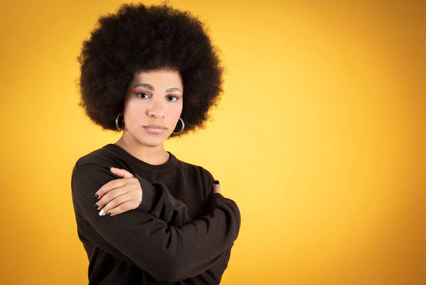 Mixed afro woman hugs herself, concept of safety, relaxation, yellow background - 写真・画像