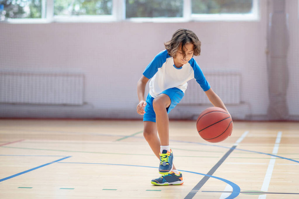 Dark-haired boy in sportswear training his basketball skills in a gym - Foto, imagen