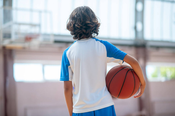 Dark-haired boy in sportswear holding a ball and looking at the basketball ring - Fotoğraf, Görsel