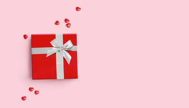 Rote Geschenkschachtel mit silberner Schleife auf rosa Hintergrund mit roten Herzen. - Foto, Bild