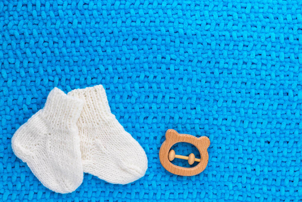 Mavi bebek ekose üzerinde bir çift şirin beyaz örgü bebek çorabı ve tahta ip ayısı. Yumuşak battaniye. Çocuk doğurmak. Yeni doğan kavramı. Düz konum, kopyalama alanı olan üst görünüm. - Fotoğraf, Görsel