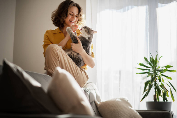 Kaunis iloinen nuori nainen söpö harmaa kissa sylissään kotona sisustus, rakkaus lemmikkejä - Valokuva, kuva