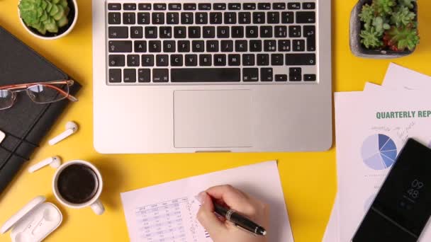 Σύγχρονο γραφείο κίτρινο γραφείο και τα χέρια των γυναικών των επιχειρήσεων γράφοντας στην έκθεση top view. Καλλιεργημένη βολή - Πλάνα, βίντεο