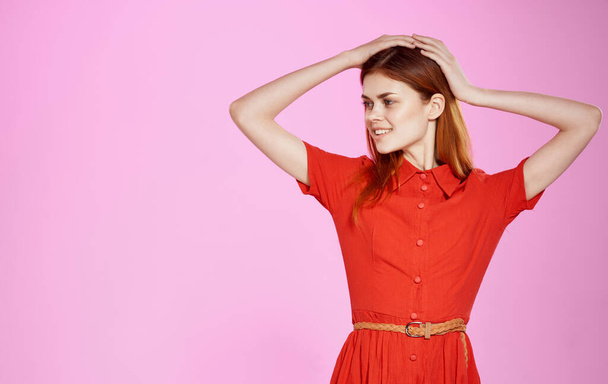 Charming woman in a red dress on a pink background gestures with her hands Copy Space - Foto, imagen