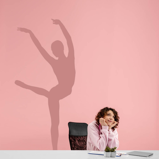 Young woman dreaming about future in big sport during her work in office. Becoming a legend. Shadow of dreams on the wall behind her. Copyspace. - Foto, Imagen