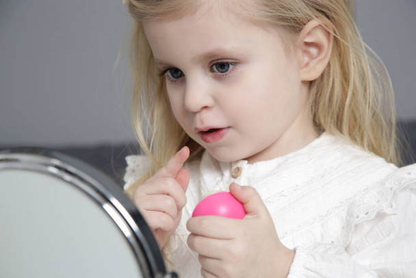 Adorable toddler girl with lip balm in front of mirror. - Foto, imagen