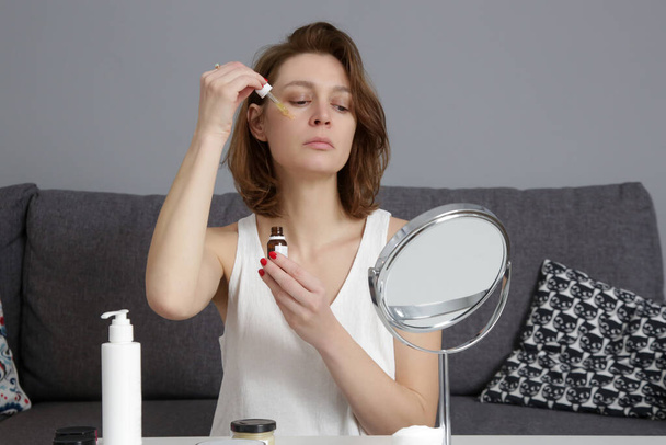 Nainen, joka käyttää ihonhoitotuotteita peilin edessä kotona. Kotielämä, kotikylpylä, itsehoito ja hemmottelu käsite. - Valokuva, kuva