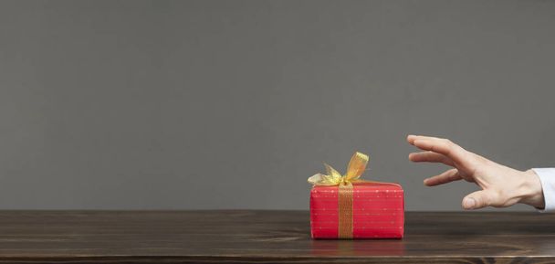Una mano busca un regalo en un paquete rojo con un lazo. Día de San Valentín. Regalo de amor - Foto, imagen