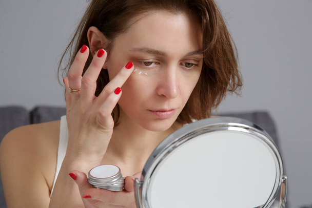 Femme utilisant des produits de soins de la peau devant le miroir à la maison. Vie domestique, spa à domicile, concept d'autosoin et de soins. - Photo, image