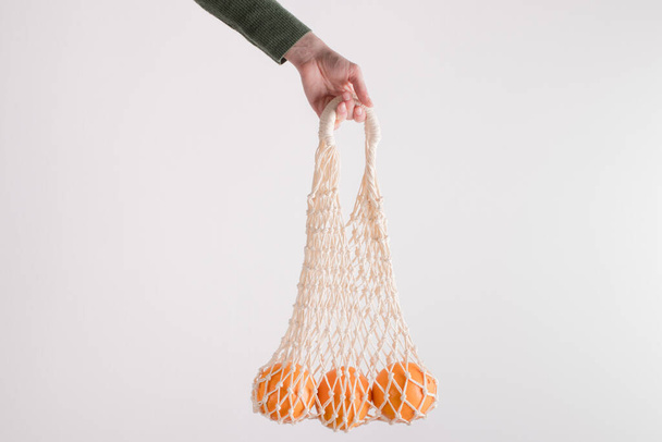 Mesh bag with oranges in female hand. Modern reusable shopping, zero waste. - Fotó, kép