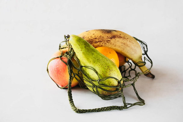 čerstvé reálné ovoce bez retuše v síťované tašce na bílém pozadí, rozumné opětovně použitelné použití věcí, filosofie pohody, selektivní zaměření - Fotografie, Obrázek