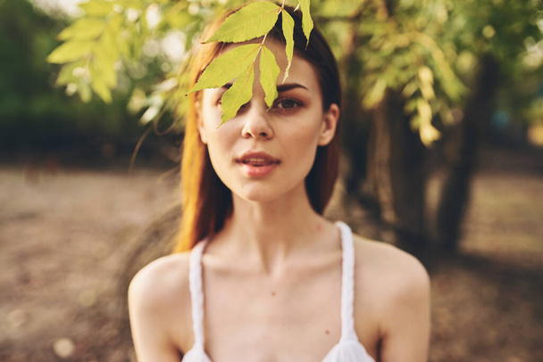 mooie vrouw in witte jurk buiten in de tuin en groene bladeren van bomen - Foto, afbeelding