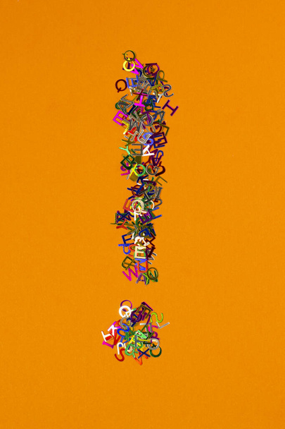 Bright multicolored small letters scattered shape exclamation mark on orange background - Photo, Image
