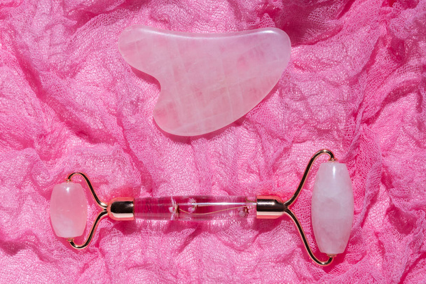 Pink Gua Sha gezichtsmassage gereedschap. Rozenkwarts jade roller op roos achtergrond - Foto, afbeelding