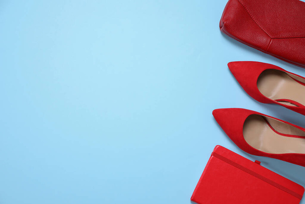 Red shoes, bag and notebook on light blue background, flat lay. Space for text - Foto, Imagen