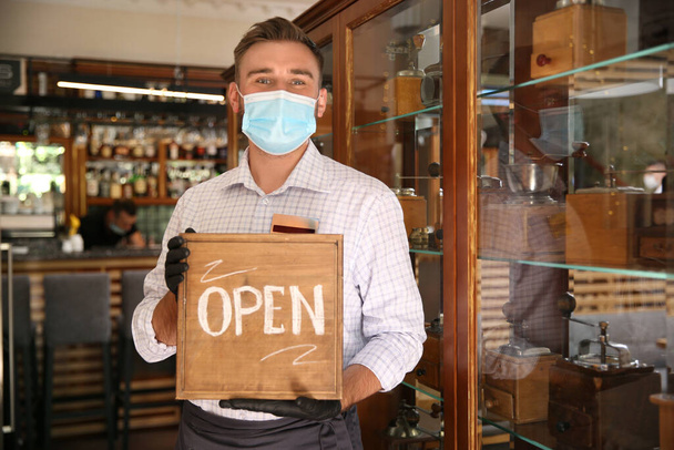 Waiter holding OPEN sign in restaurant. Catering during coronavirus quarantine - Fotoğraf, Görsel