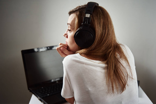 Женщина слушает онлайн курсы по наушникам, дистанционному образованию. Ленивый и рассеянный сотрудник на удаленной работе - Фото, изображение
