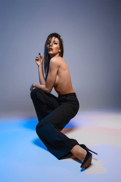 Brunette in wide black trousers covers her breasts - Fotó, kép