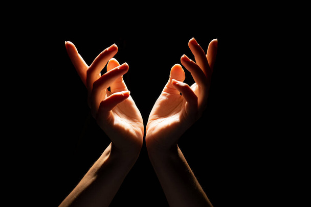 Beautiful folded hands with light on top, black background. Prayer or creating a miracle. - Foto, Imagem